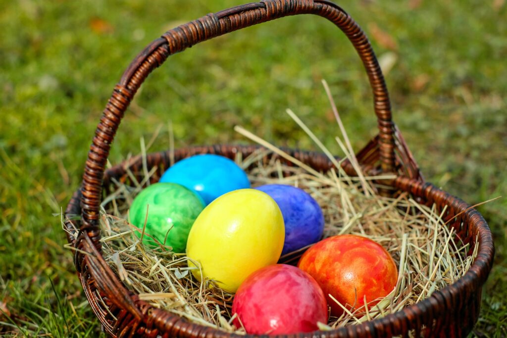 Bunte Ostereier im braunen Flechtkorb auf grünem Gras.