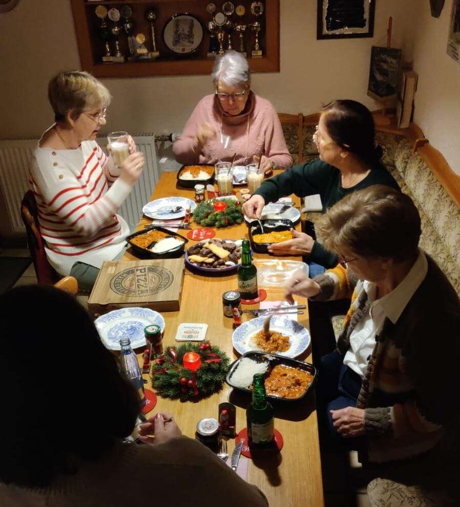Auf dem Bild sind fünf Frauen zu sehen, die gemeinsam um einen Tisch sitzen und zusammen essen. Der Tisch ist weihnachtlich geschmückt.