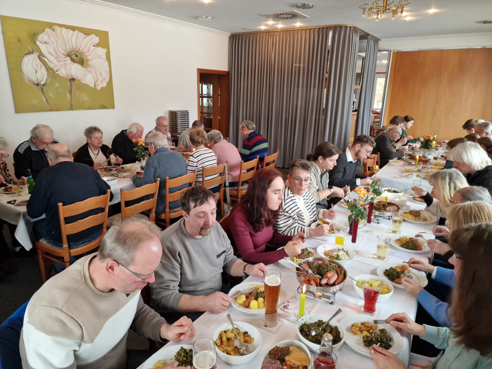 Auf dem Bild sind viele Personen zu sehen, die um Tische sitzen und Braunkohl essen.