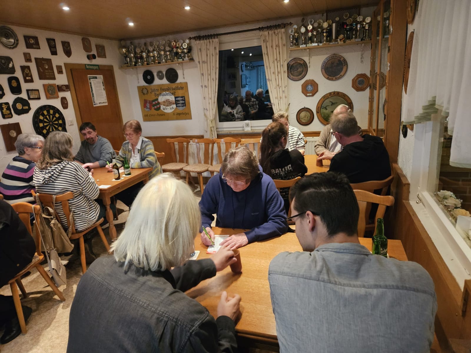 Es sind mehrere Personen zu sehen, die um Tische sitzen und knobeln.