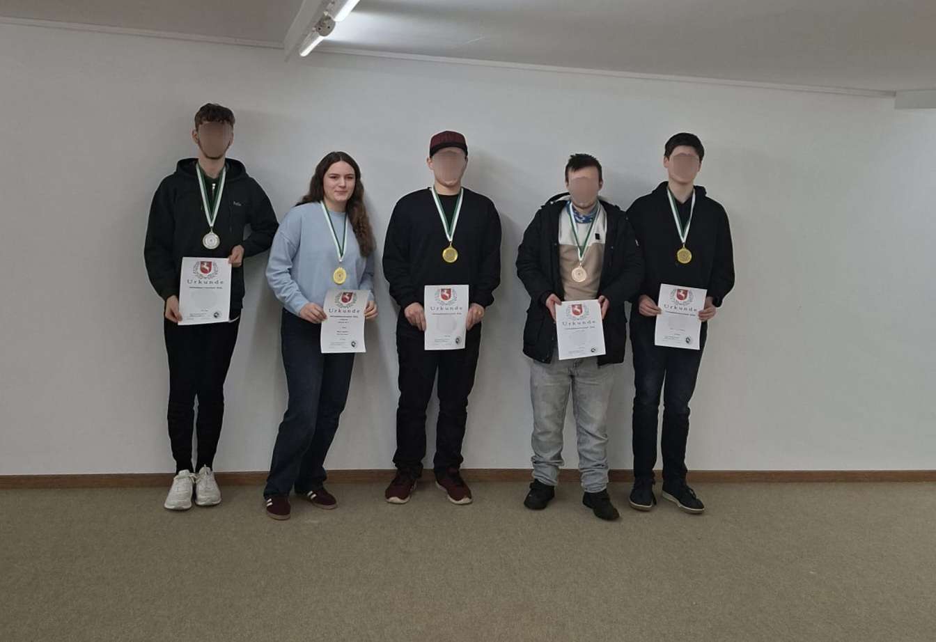Auf dem Bild posieren vier Männern und eine Frau. Sie halten Urkunden in der Hand und haben Medaillen um.