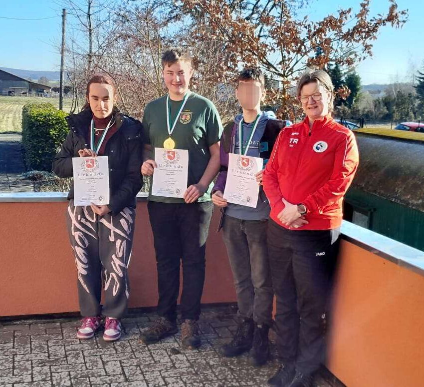 Auf dem Bild posieren 4 Personen für ein Foto. Dabei haben drei Personen eine Medaille um und halten eine Urkunde in der Hand.