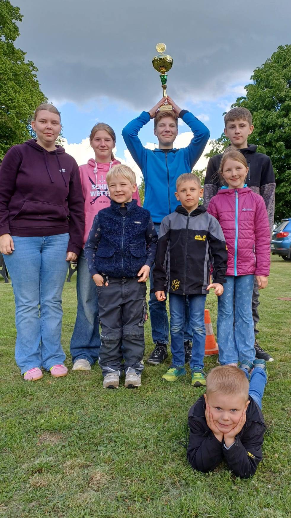 Auf dem Bild sind 8 Jugendliche zu sehen, die gemeinsam für ein Gruppenbild posieren und in der Mitte wird ein Pokal hochgehalten.