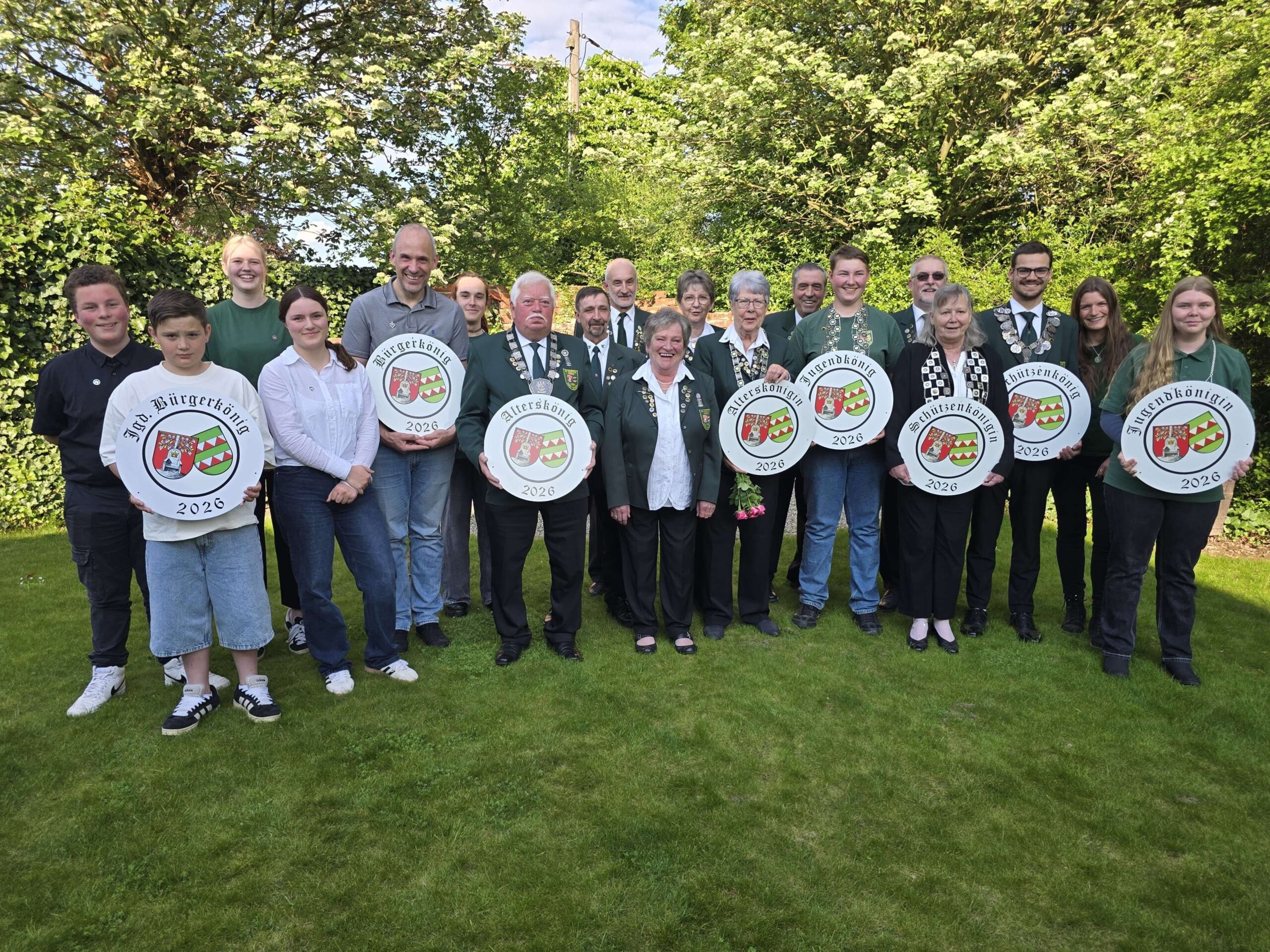 Die Könige, Königinnen und Edeldamen, Edelfräulein, Ritter und Kaiser stehen für ein Gruppenfoto zusammen und präsentieren ihre Scheiben. Alle tragen die Vereinsuniform von grünen Jacken, weißen Blusen oder Hemden oder grüne Pullover/T-Shirts und schwarze Hosen.