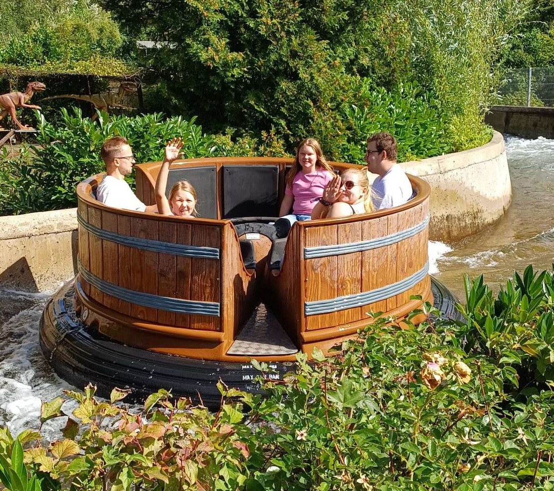Auf dem Bild sind 5 Personen auf der Rafting-Bahn im Rasti-Land, lachen und winken in die Kamera